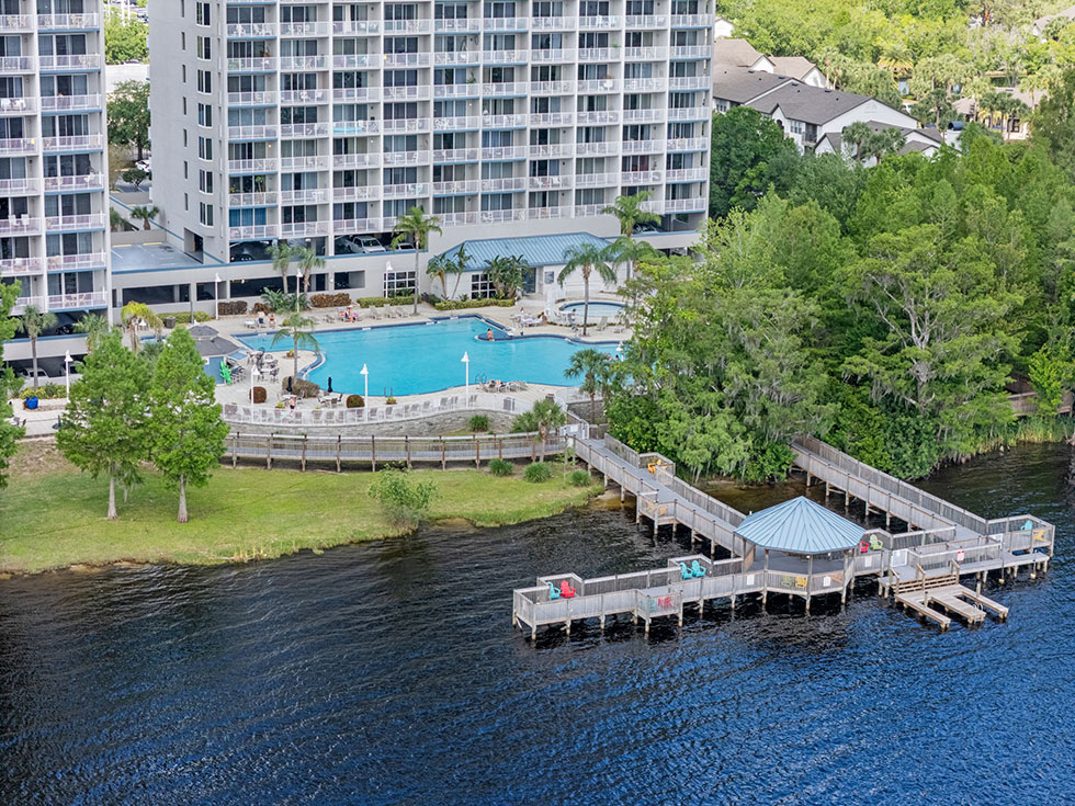 Resort-style amenities including heated pools, hot tub spa, BBQ grills, fishing docks with lounge chairs, kayak launch, arcade, tiki bar, and two gyms overlooking the pool and lake.